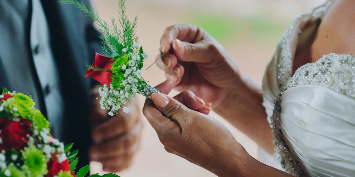 Close-up of a boutonnière being pinned to a groom's suit