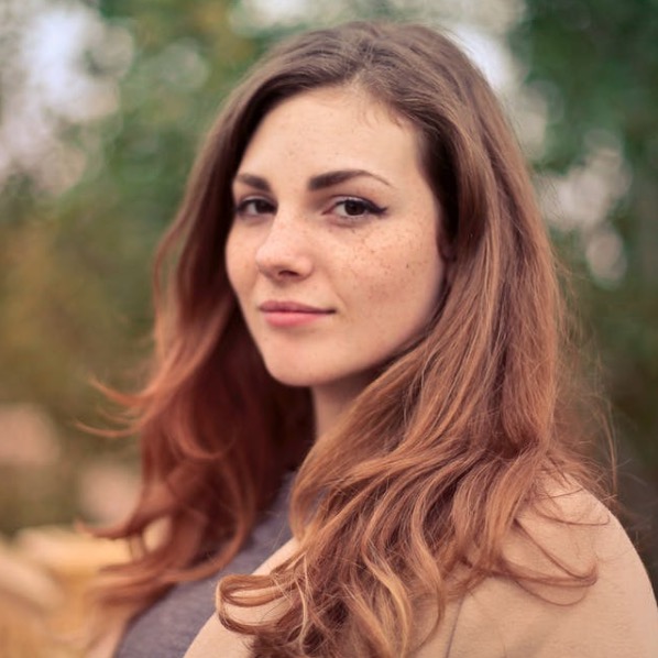 A woman with long hair and freckles smiling outdoors.