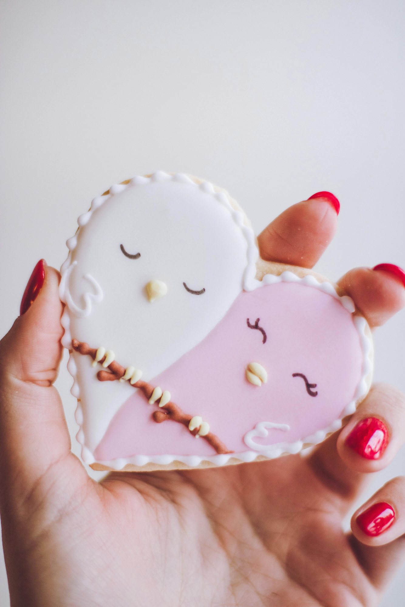 Hand-held heart-shaped cookies featuring two lovebirds
