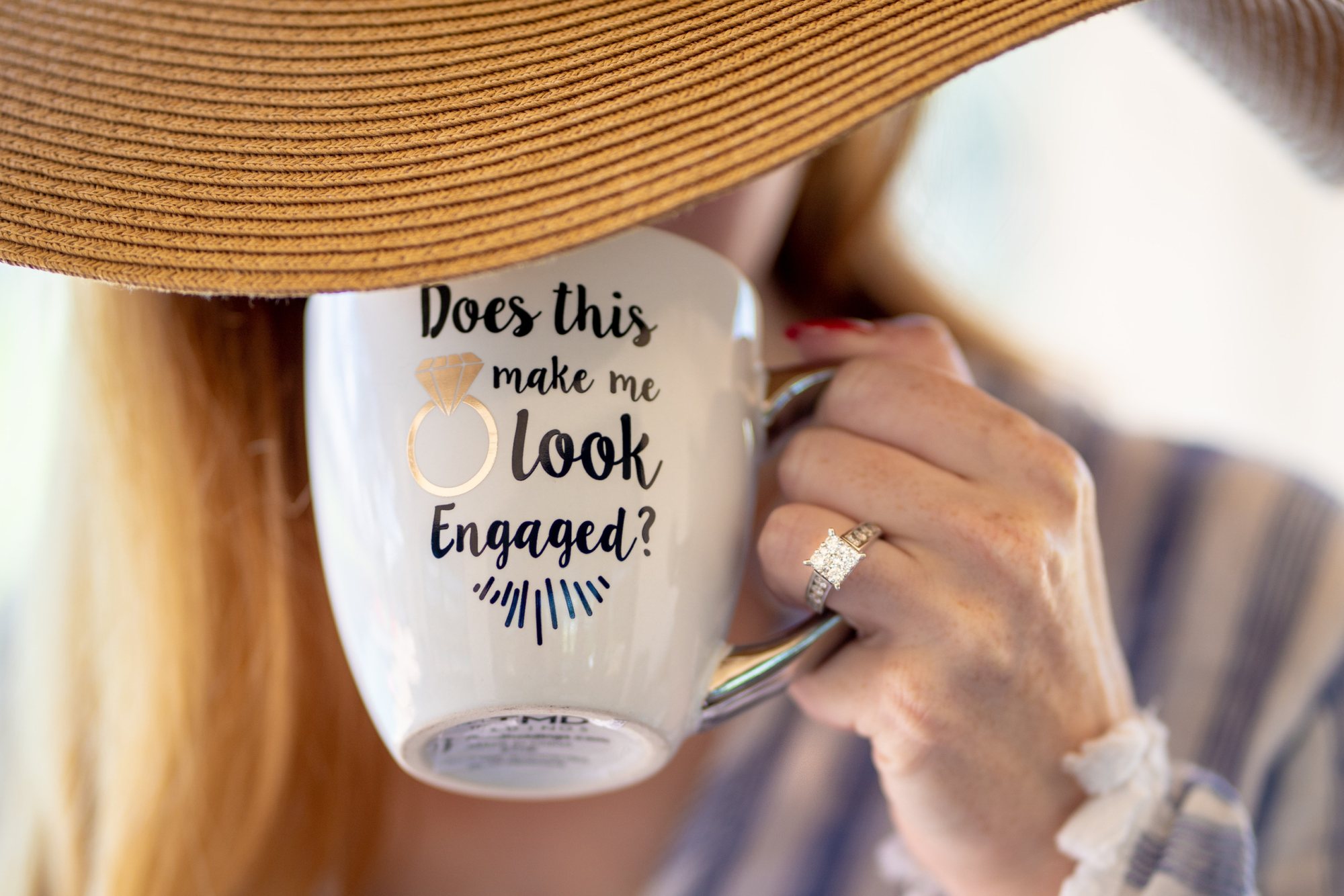 Mug with engagement ring design held by a person wearing a hat.