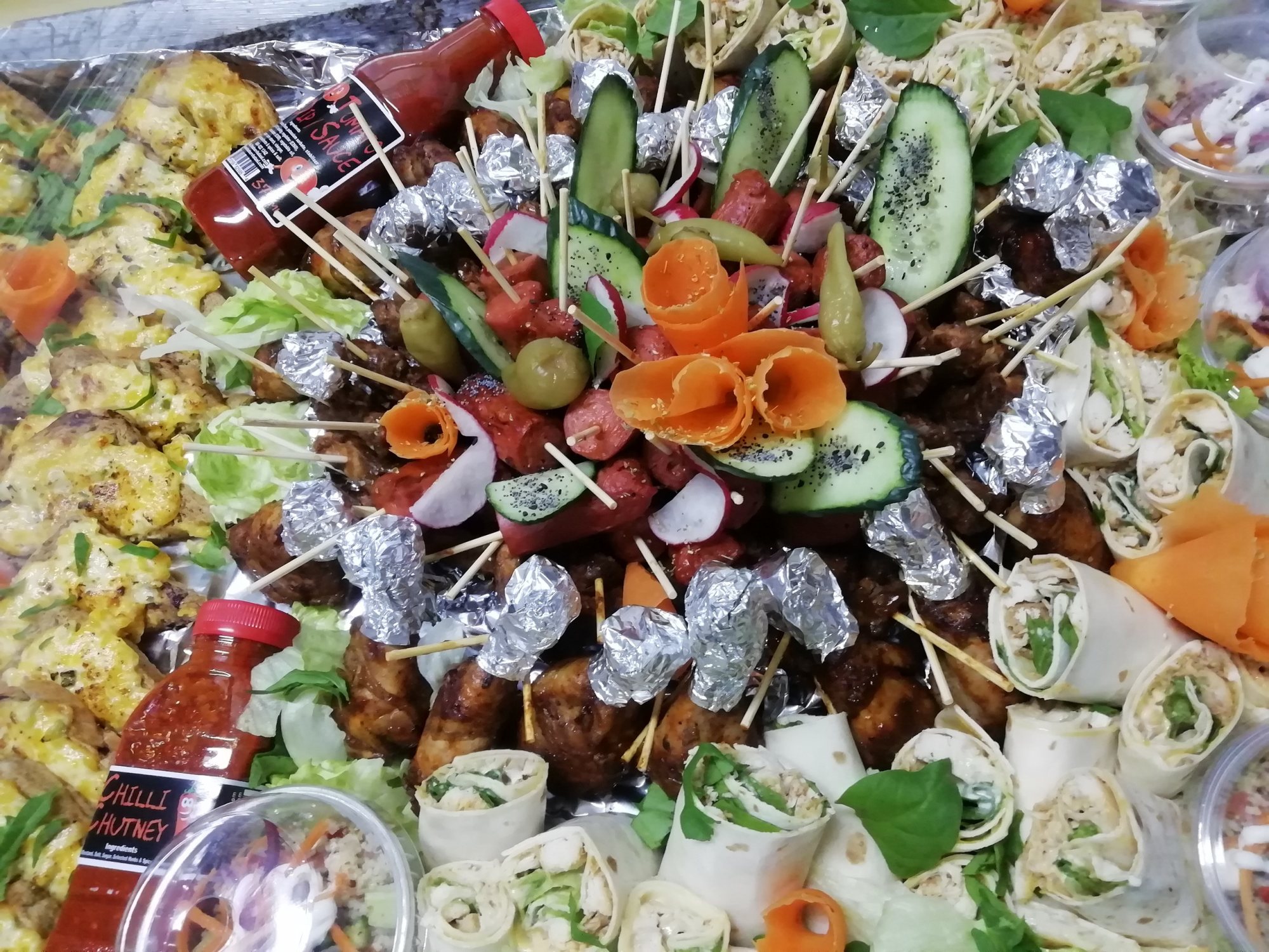 A colorful catering platter with skewers, wraps, and sauces.