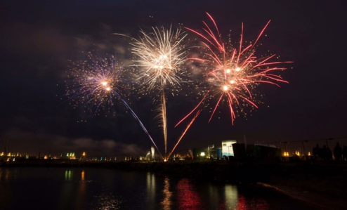 Fireworks bursting in colorful displays over a body of water at night.