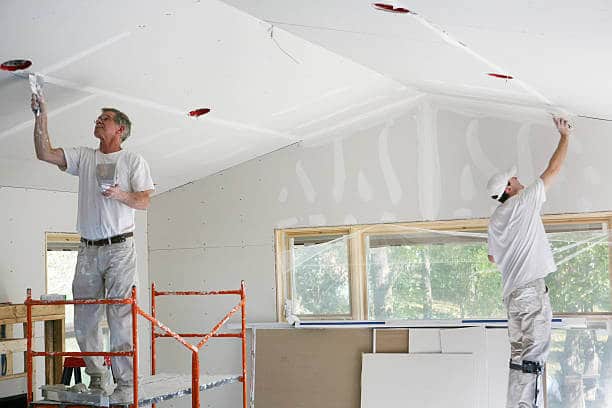 Two workers applying drywall finish in a room