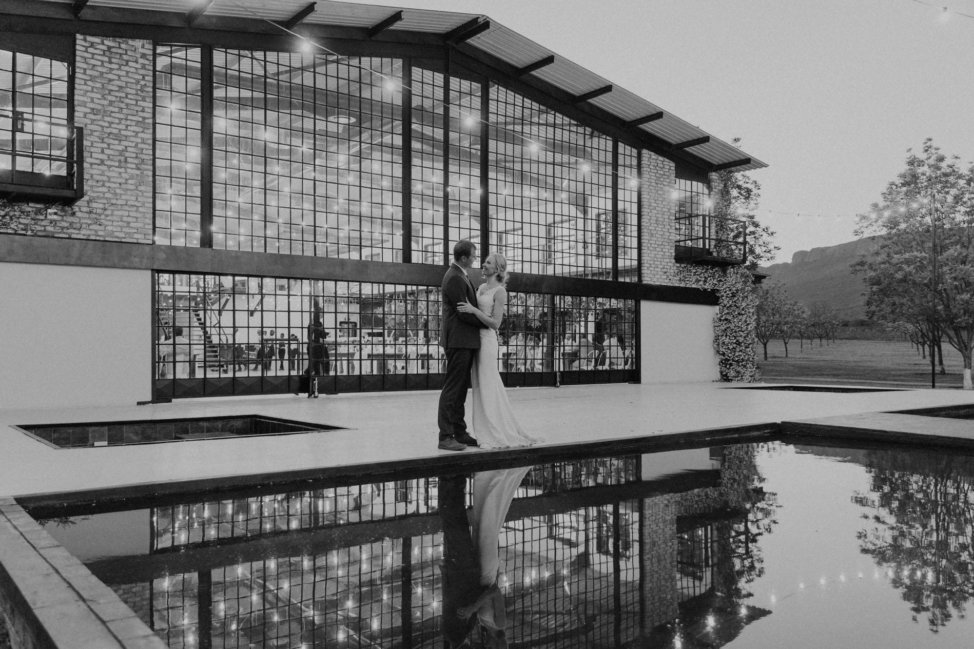 Couple standing by a reflective pond in front of a modern venue