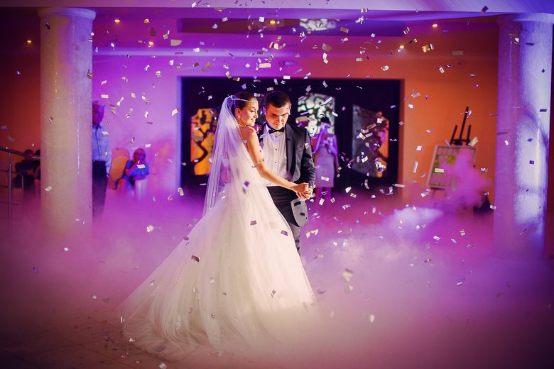 Couple dancing amidst confetti and fog at a wedding
