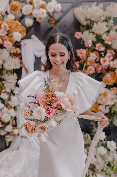 Bridal bouquet with pink and cream flowers in front of floral backdrop